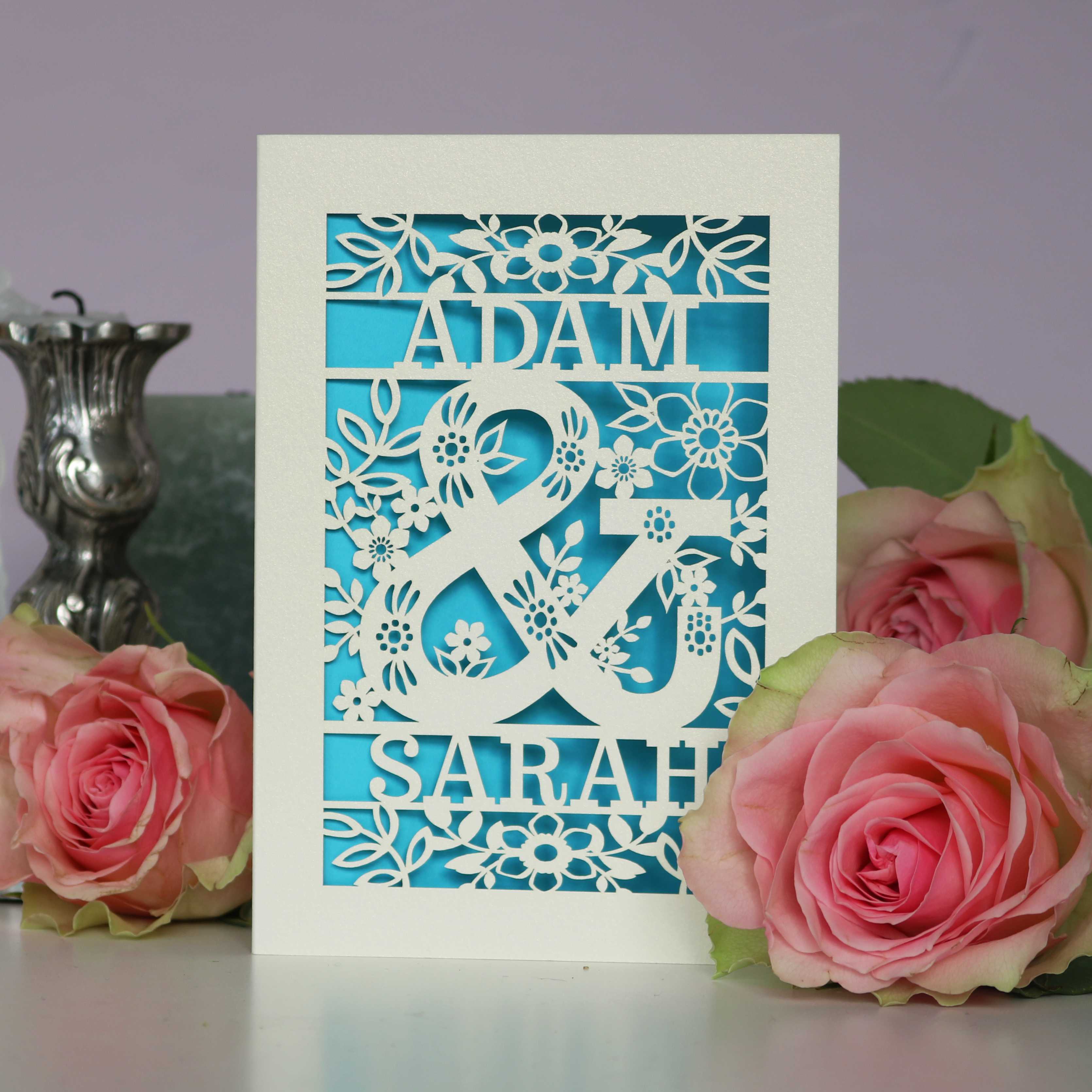 A paper cut wedding card with two names and an ampersand in the middle