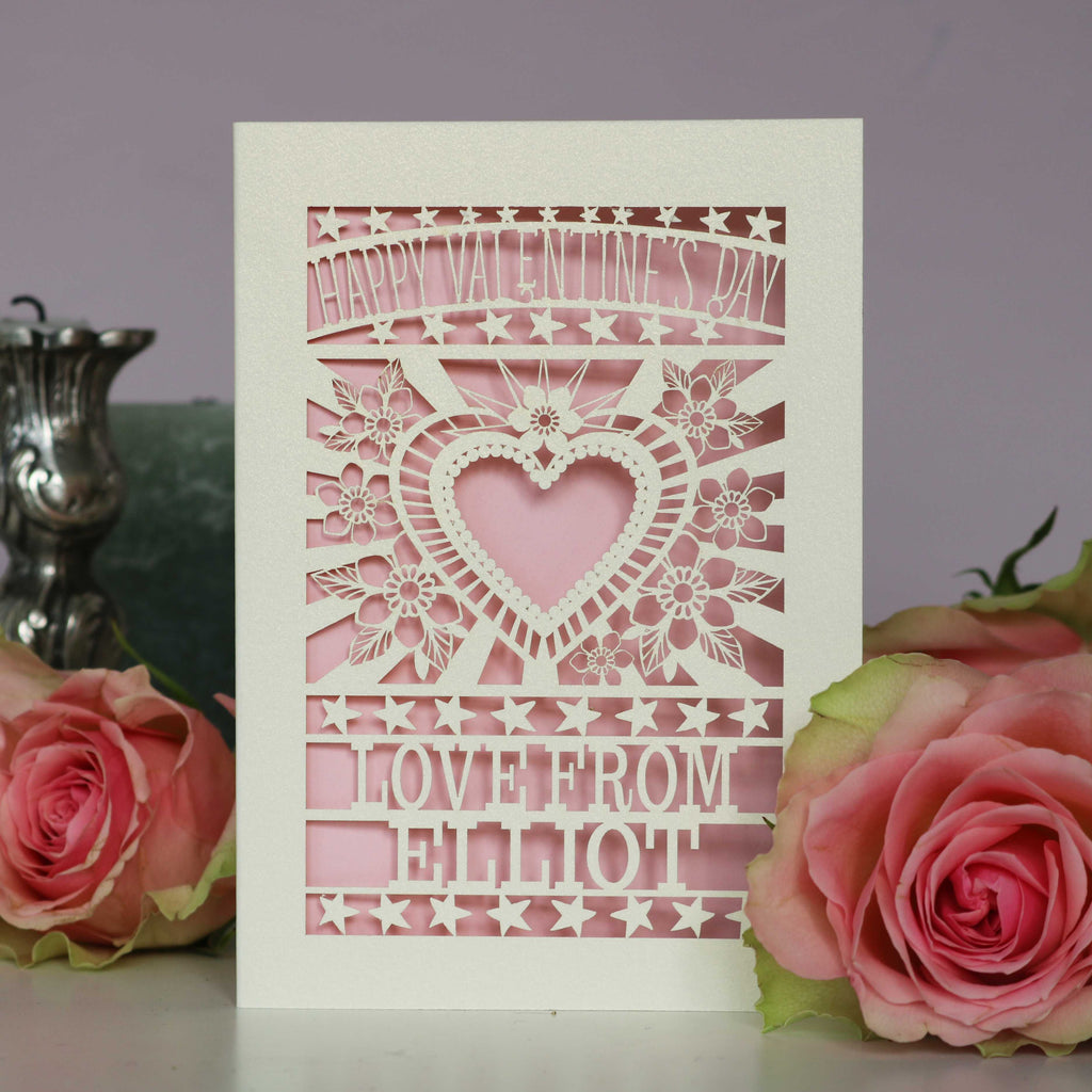 A personalised cut out Valentines card that has a heart and flowers cut out and text that says "Happy Valentine's Day, love from" and a name