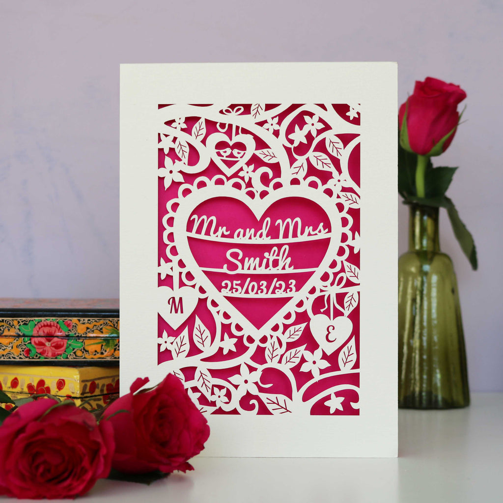 A luxury papercut wedding card showing Mr and Mrs and a surname inside a heart with a date and initials. 