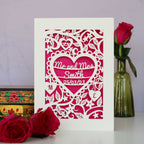 A luxury papercut wedding card showing Mr and Mrs and a surname inside a heart with a date and initials. 
