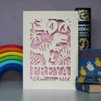 A cream and pink birthday card for a girl. This card shows a dinosaur holding balloons with a name and age personalised details. 