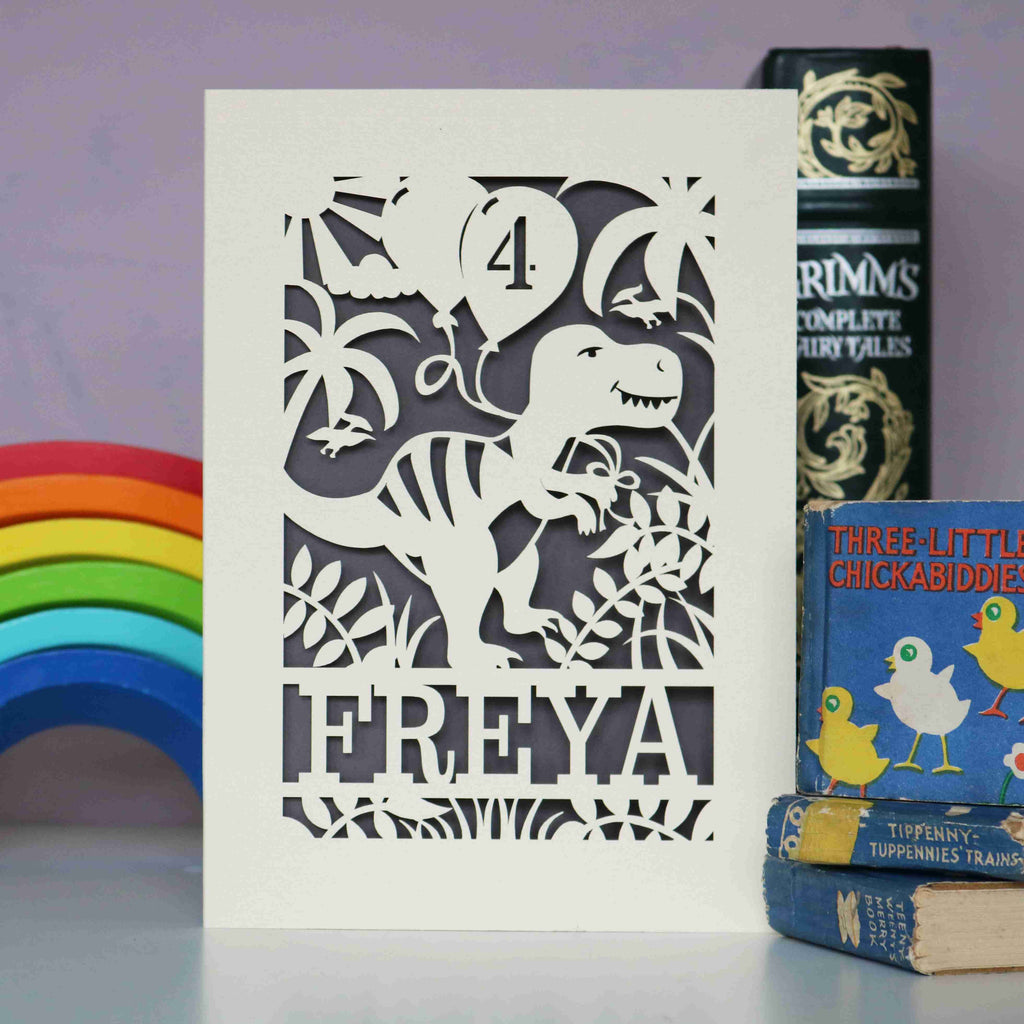 Personalised birthday cards for dinosaur fans. Image shows a laser cut dinosaur holding balloons and is personalised with an age and name.