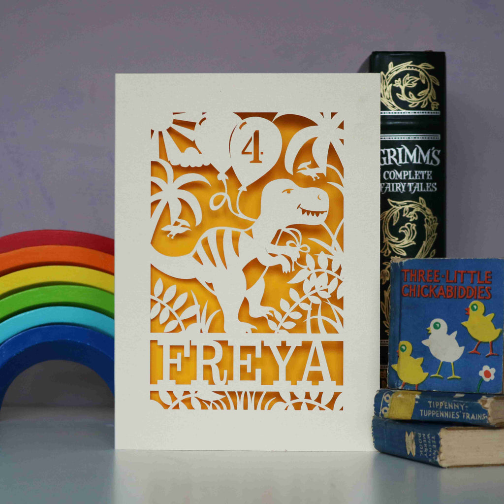 A girl's dinosaur birthday card in cream and yellow. Laser cut cards show a dinosaur holding birthday balloons