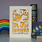 A girl's dinosaur birthday card in cream and yellow. Laser cut cards show a dinosaur holding birthday balloons