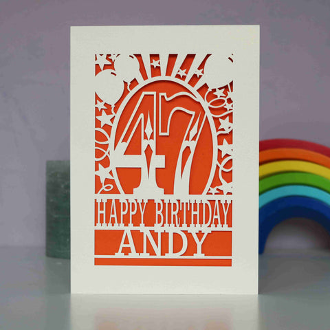 A cream paper cut birthday card cut away to reveal an orange background. Cut design is an age surrounded by stars and balloons, with the words "Happy birthday" and personalised with a name - A5 (large) / Orange