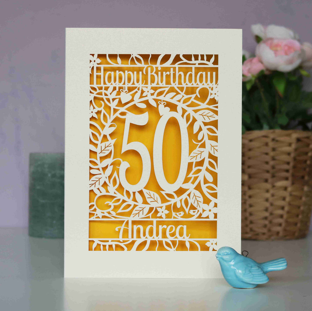A floral birthday card with an age and a name laser cut from cream card. There is a warm sunshine yellow paper behind the laser cut card.