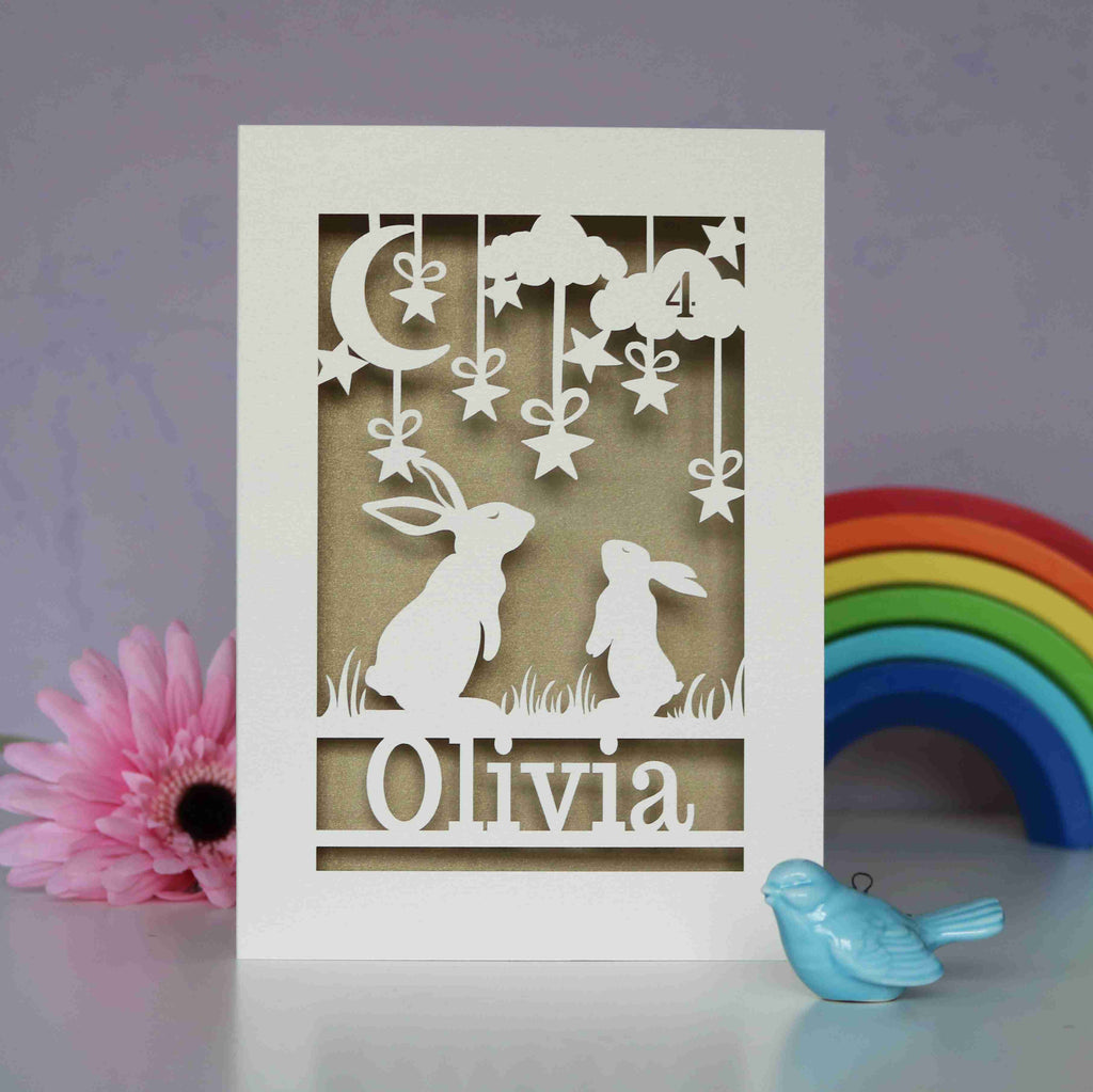 A cream and gold papercut birthday card with rabbits looking up at the moon and stars