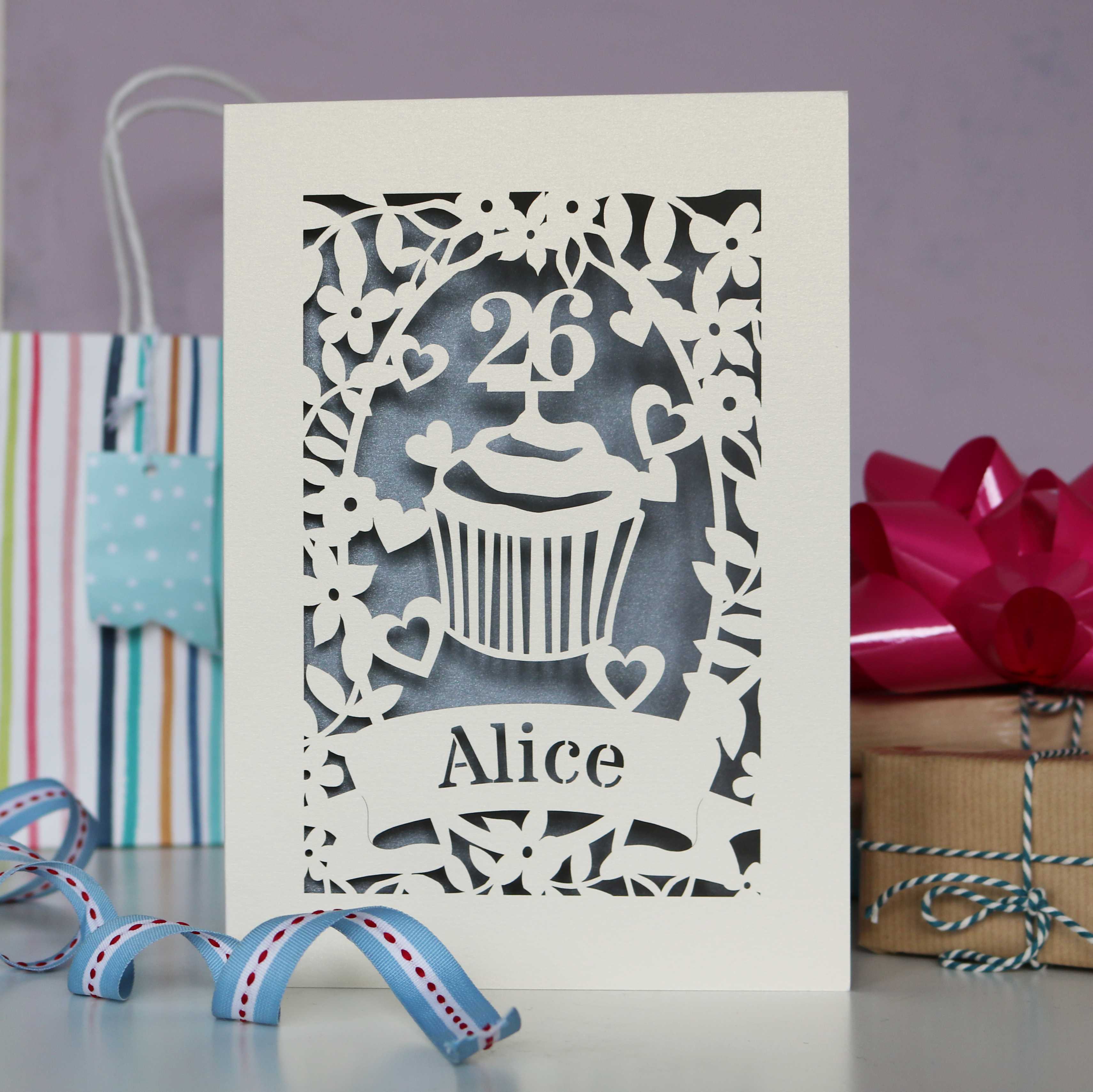 Elegant silver and cream personalised  birthday card. Shows a cupcake with an age topper, leaves, flowers and hearts all laser cut from cream card. Personalise with age and a name.