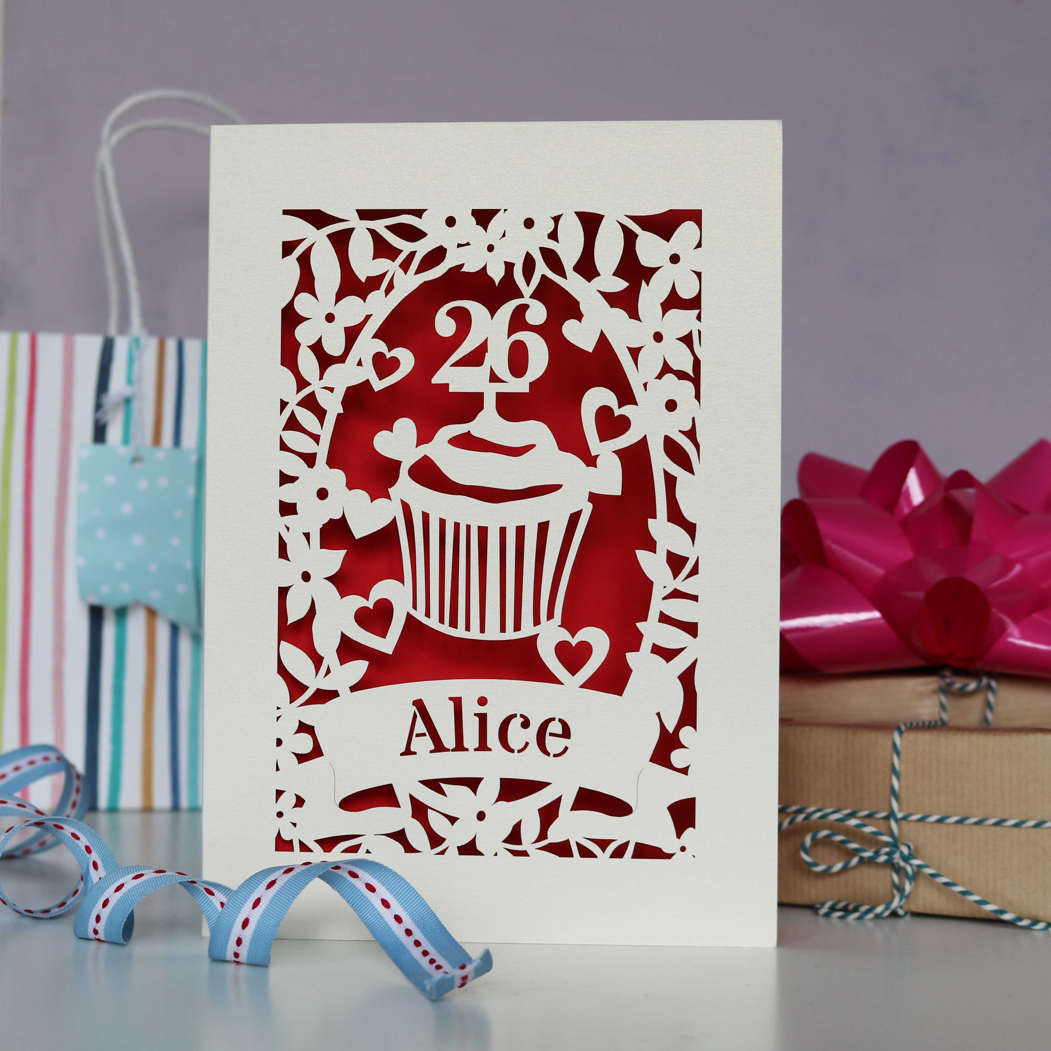 Laser cut personalised birthday card. Cup cake design with an age topper, surround with leaves, flowers and hearts. Great for the cake lover in your life. Cut from cream card with a red insert paper.