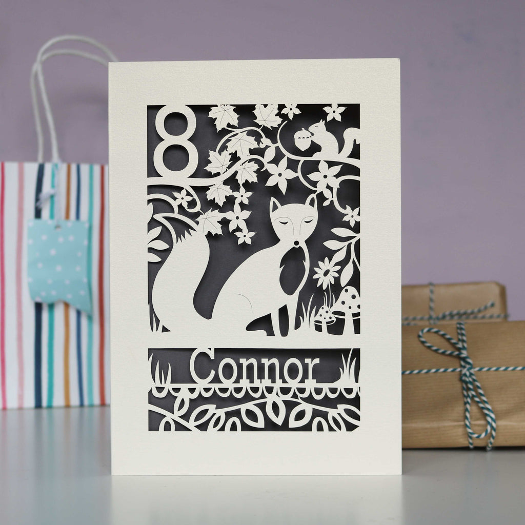 This is a boring job. I have run out of ways to describe a fox birthday card. This is an image of a birthday card. There is a fox on it. And flowers. And leaves. And a squirrel holding an acorn. It's cute. There is a name at the bottom. and and age at the top. Can I go home yet?