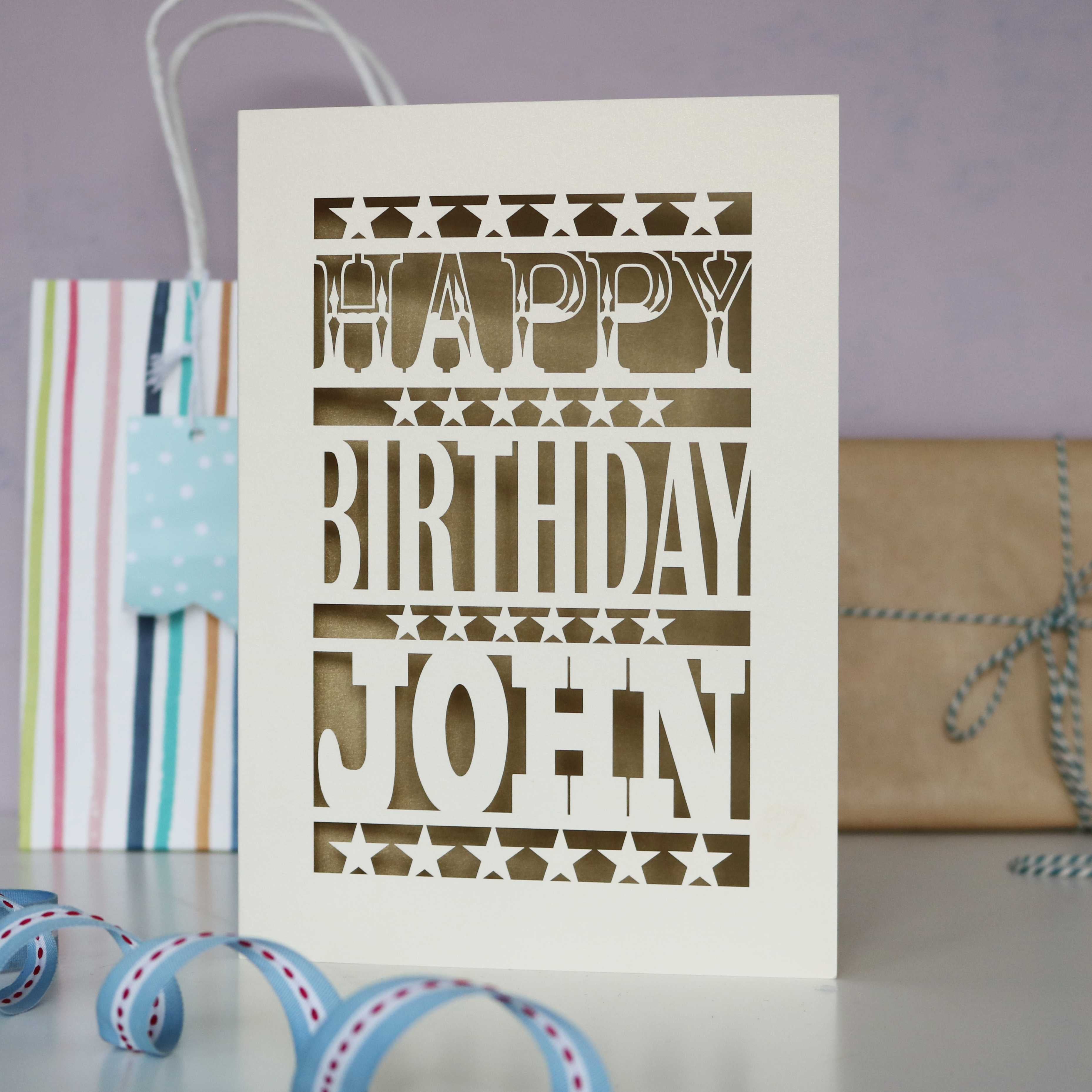 Cream laser cut card for birthdays, saying happy birthday with a name, and gold leaf paper behind cut out card