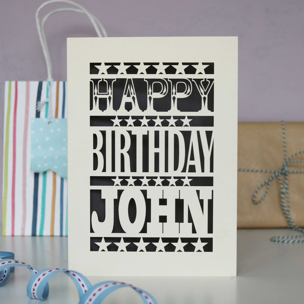A man's birthday card, personalised with a name and laser cut from cream and dark grey.
