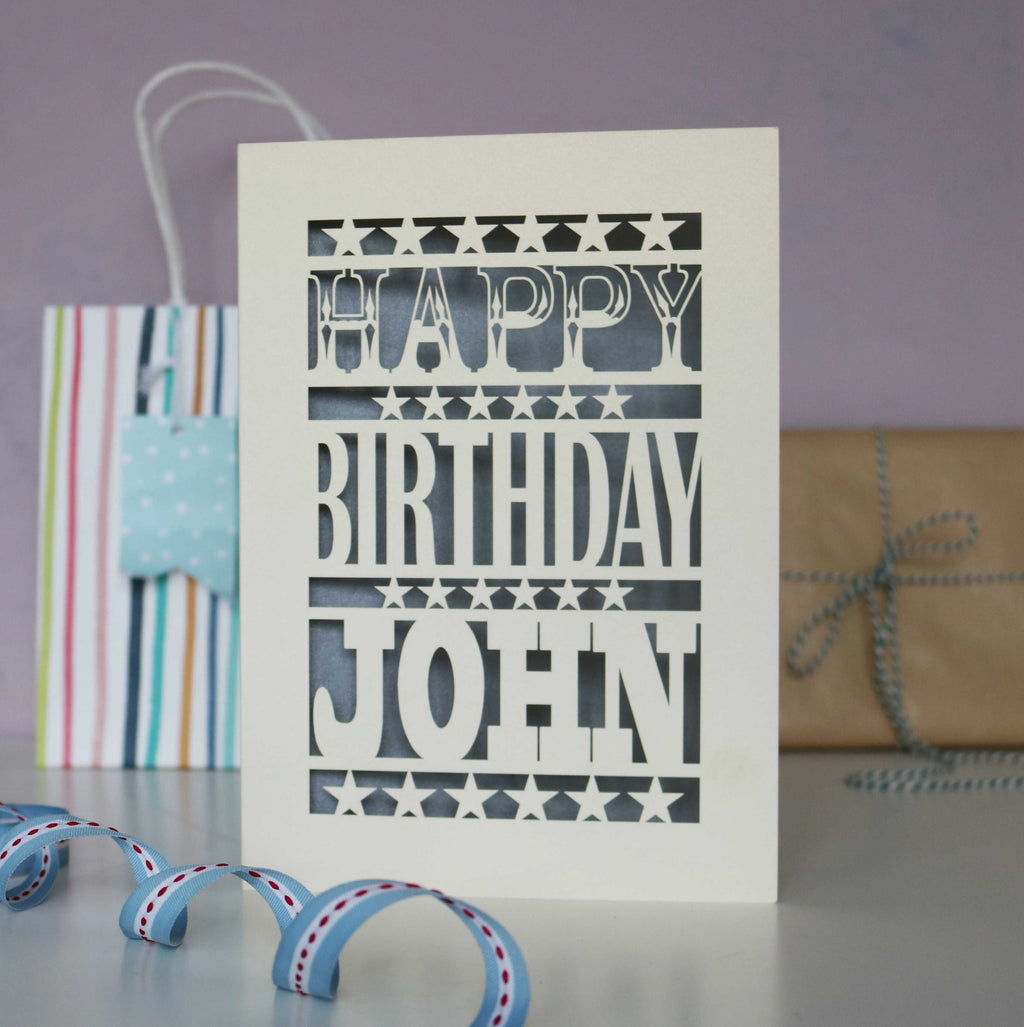 A personalised laser cut birthday card for a man. Stars and bold chunky text that says "Happy Birthday Daniel." Card is cream and silver.