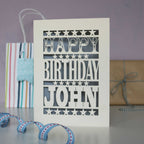 A personalised laser cut birthday card for a man. Stars and bold chunky text that says "Happy Birthday Daniel." Card is cream and silver.