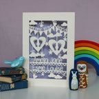 Sweet papercut personalised welcome to the world twins card.  Two sets of tiny feet cut from two hearts, surrounded with clouds, stars and hearts.  Personalise with both babies names. Shown in cream card  and finished with a lilac background.