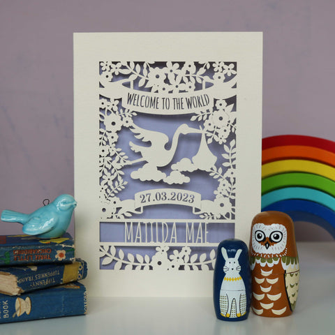 A laser cut cream and lilac new baby card personalised with the baby's name and date of birth. The top of the card reads "Welcome to the World" and the centre of the design is a stork surrounded by leaves and flowers. - A6 (small) / Lilac