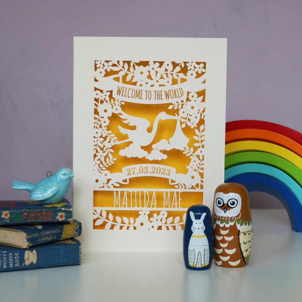A cream and yellow new baby card personalised with a date and name. Card reads "Welcome to the world" at the top inside a banner.