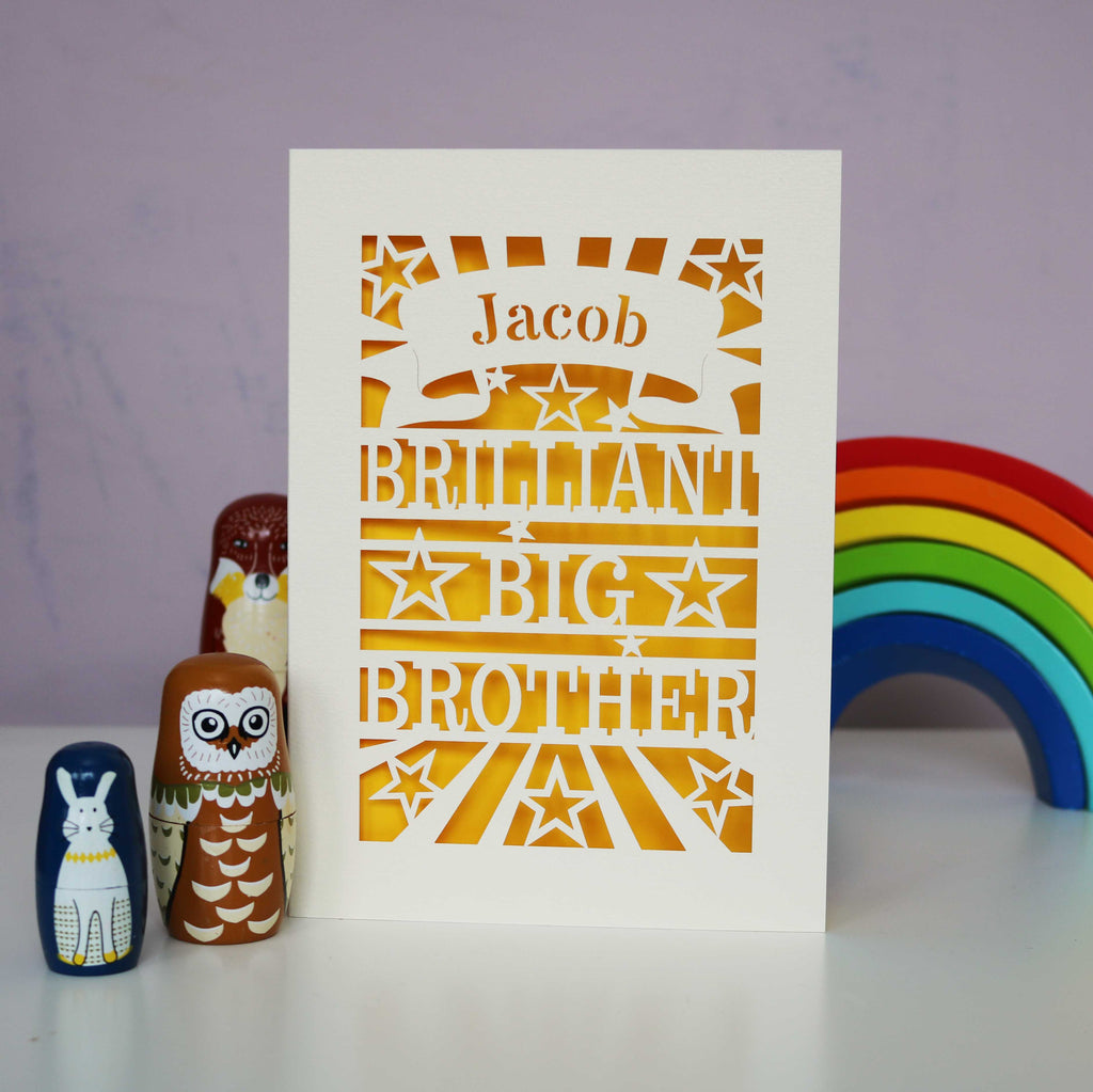 A laser cut card with "Jacob, Brilliant Big Brother", on a desk with wooden toys