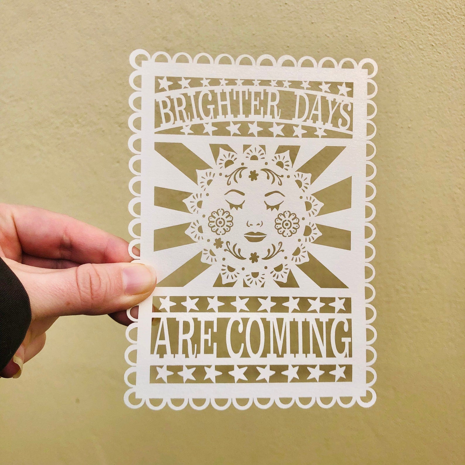 A cream coloured laser cut postcard featuring the words Brighter Days Are Coming, against a yellow background.