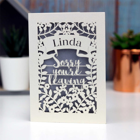 Gorgeous personalised lasercut leaving card. With a banner for the leaver's name over the words "Sorry you're leaving" and lots of flowers.  Cream card with a silver background. - A5 / Silver