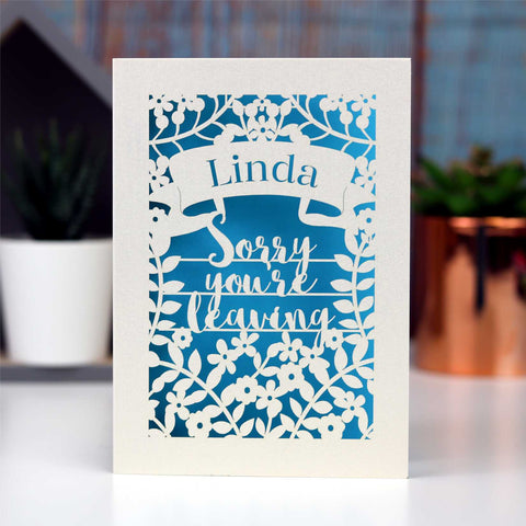 Personalised leaving card showing the words "Sorry you're leaving" with a banner to personalise and surrounded with flowers. All cut from cream card and finished with a peacock blue insert paper. - A5 / Peacock Blue