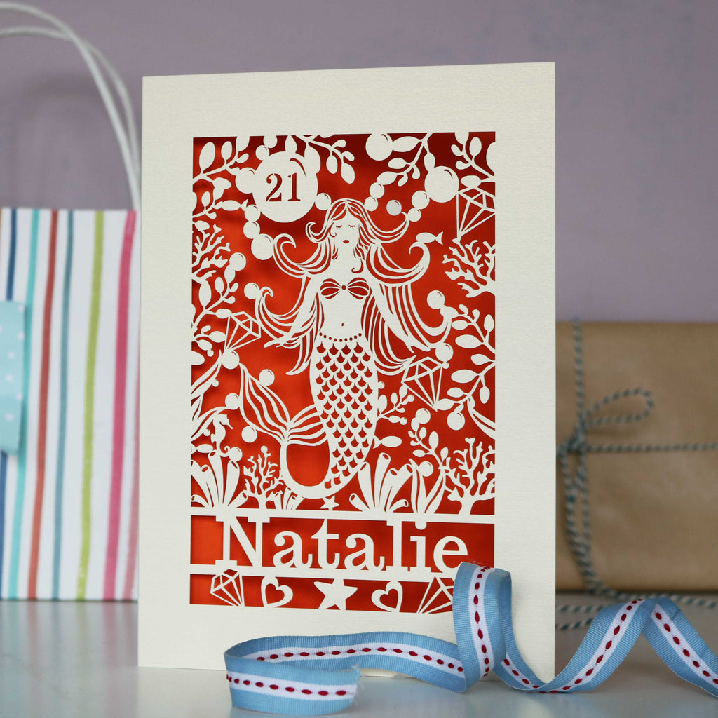 A cream and orange papercut birthday card for her. Mermaid is laser cut with bubbles, gems and fish around her. Card is personalised with a name and age.