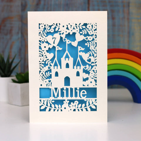 A personalised birthday card for granddaughters with a princess castle and a name and age. Card is cream with a blue paper insert.  - A5 / Peacock Blue