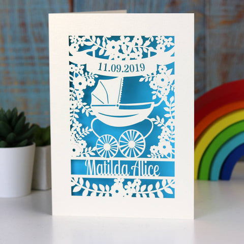 Laser cut cards for new babies. This one is personalised with a date in a banner at the top, a vintage silvercross pram surrounded by flowers and a name underneath.  - A5 / Peacock Blue