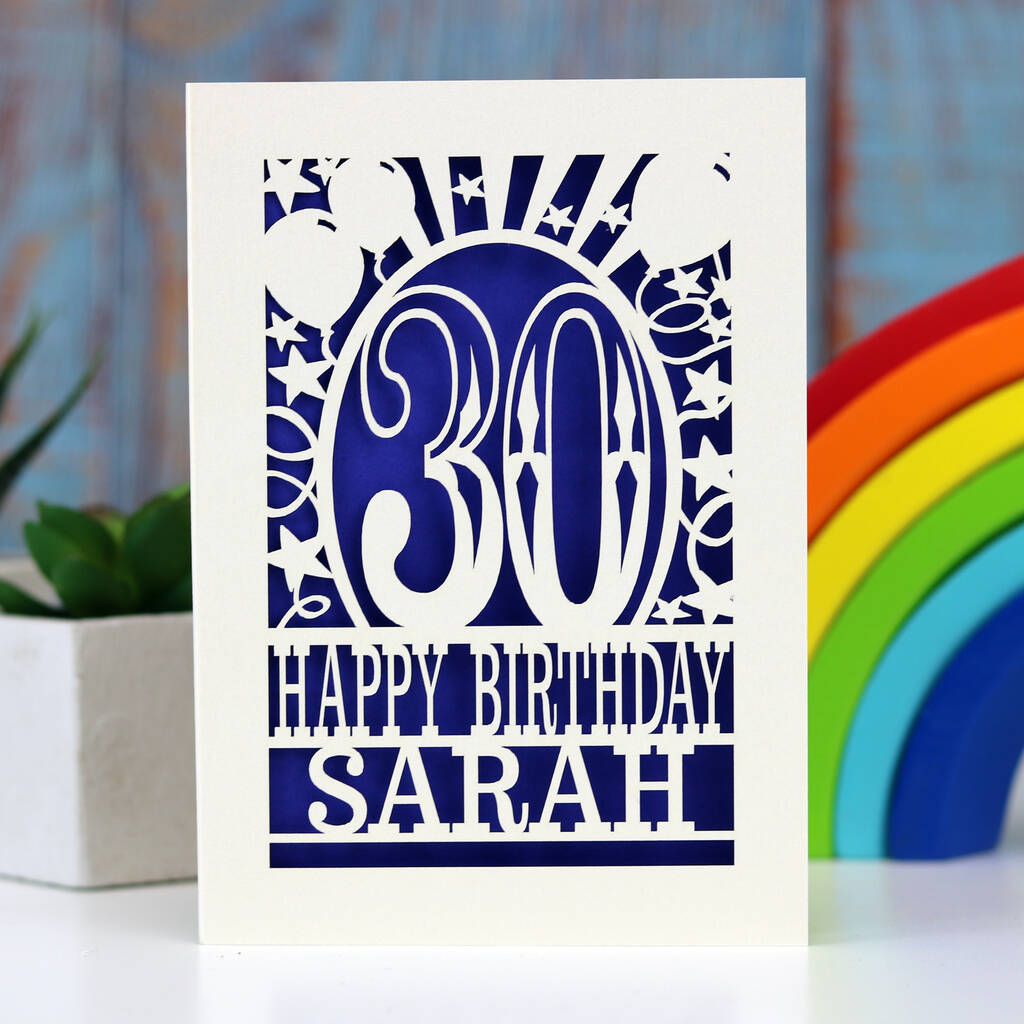A cream personalised paper cut birthday card cut away to reveal a violet background. Cut design is an age surrounded by stars and balloons, with the words "Happy birthday" and a name underneath