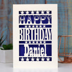 A paper cut birthday card for him. Happy Birthday Daniel is written on the front of the card. Card can be personalised with any name. Stars separate each line of text and background is violet.