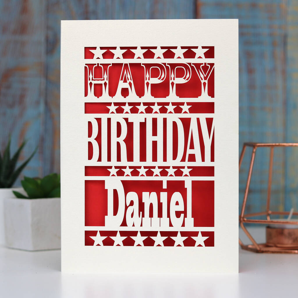 A birthday card with stars and the words Happy Birthday in cream and a name underneath. Red paper sits behind the laser cut design
