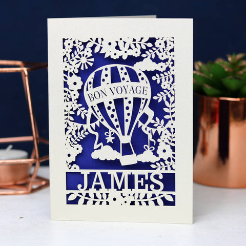 Lasercut card with a dark blue insert background. Shows a hot air balloon floating between the leaves and clouds. Personalised with the name of the traveller. - A5 (large) / infra violet