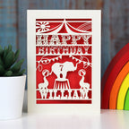 Elephant and seals at the circus on this fun personalised papercut birthday card. Shown cut from cream card with a bright red insert paper. Personalised with age and name.