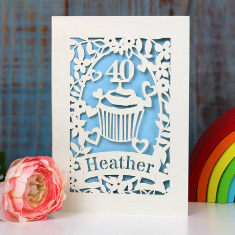 Pretty cupcake design laser cut personalised card. Shows a cupcake with an age topper, heart, leaves and flowers. Can be personalised with a name and age. Laser cut from cream card and finished off with a pale blue background. - A5 / Light Blue