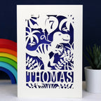 A cream and violet birthday card for son. Personalised cards feature a dinosaur holding a balloon