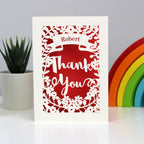 Gorgeous cream papercut card with a red background.  Shows a banner across the top to personalise with a name and "Thank you" in large script surrounded with flowers.