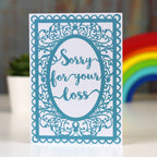 A sympathy card with a blue ornate border and the text 'Sorry for your loss' displayed in a cursive font inside a oval shape.